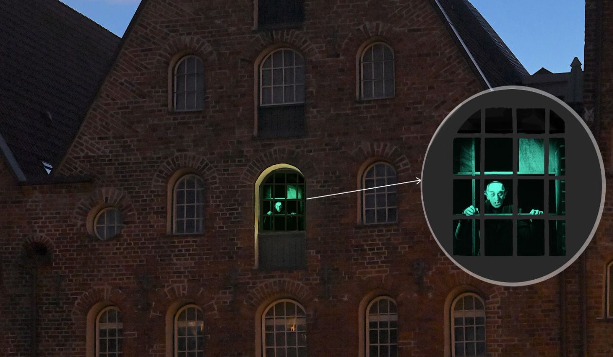 Zu sehen ist die Figur Nosferatu aus dem gleichnamigen Film von Friedrich Wilhelm Murnau aus dem Jahr 1922. Er ist grün angeleuchtet und schaut aus einem Fenster des Lübecker Salzspeichers heraus.