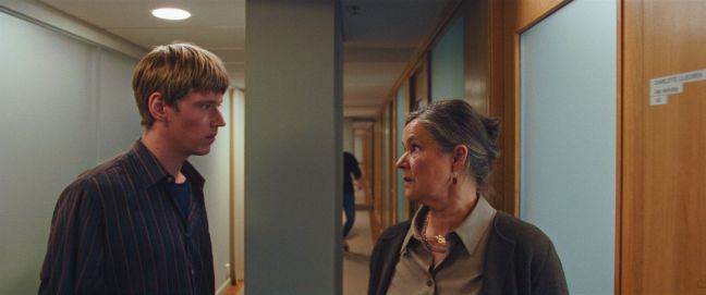 Johannes steht Charlotte im Büro gegenüber, sie schauen sich an