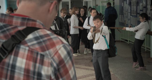 Ein Kind zielt auf Pavel mit einem Waffenimitat, im Hintergrund „spielen“ weitere Kinder.