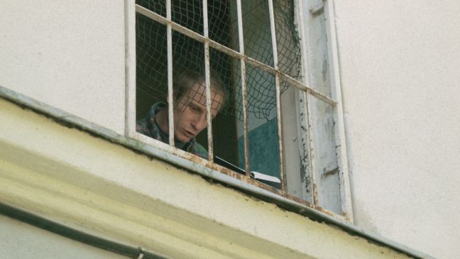 Ein Mann hinter Gitter liest am Fenster aus einem Heft