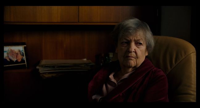 Dargmar im Dunkeln auf ihrem Sessel, im Hintergrund ein Foto mit ihrem Mann