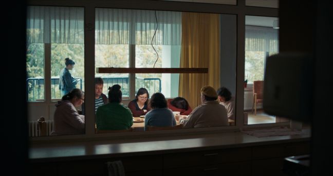 Luisa sitzt mit der Wohngruppe am Tisch, den Kopf auf der Tischplatte