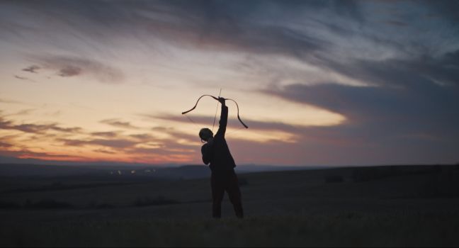 Vor Sonnenuntergang steht ein Mann mit Bogen und zielt in den Himmel