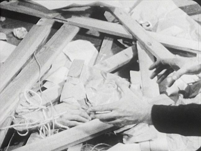 Hände zwischen Holzlatten, Papieren und Schnüren