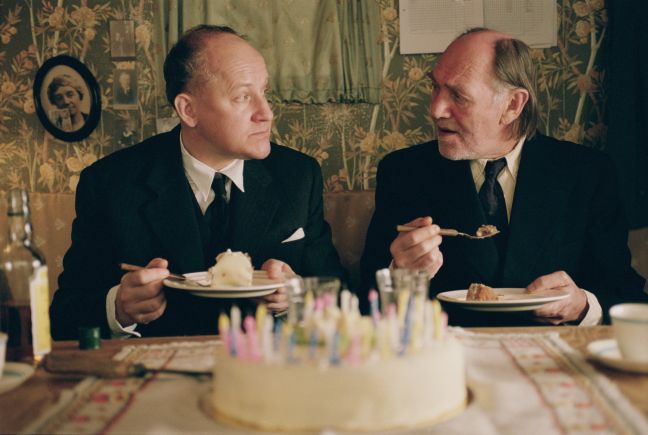 Folke und Isak im Anzug schauen sich beim Geburtstagskuchenessen an