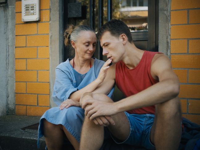Patty neben einem jungen Mann, sie berührt ihn am Mund