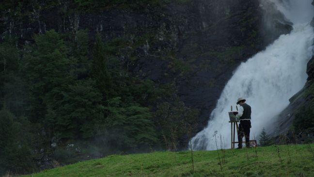 Astrup malt auf einer Wiese stehend einen Wasserfall
