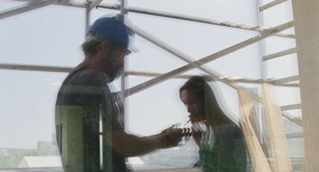 Ilona und Oleg in der Spiegelung des Fensters, Oleg zündet Ilonas Zigarette an