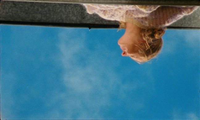 Das Bild ist kopfüber, eine blonde Frau kneift in der Sonne die Augen zusammen, blauer Himmel