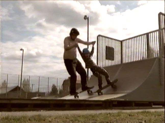 Vater auf Skateboard hilft dem Sohn beim Skateboarding fahren auf einer Halfpipe