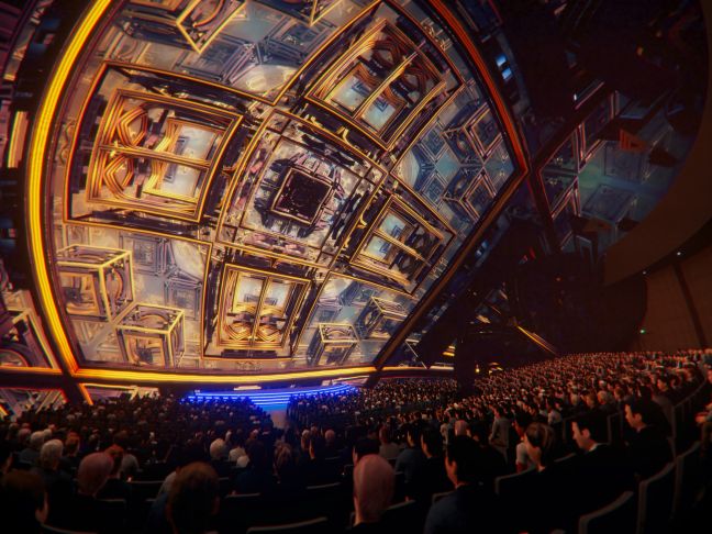 In einem großen Saal vor vollem Publikum sieht man fliegende einzelne Quadrate aneinander, in denen weitere sind