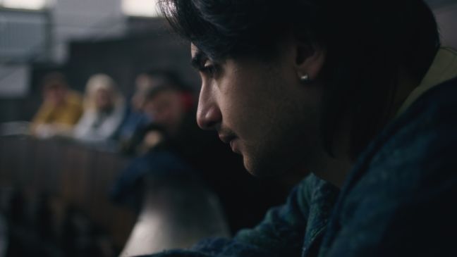 Samir blickt ernst den Rang hinab, im Hintergrund stehen mehrere Personen zusammen