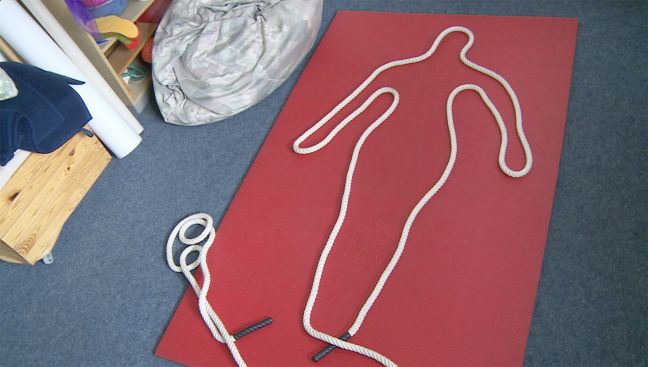 Auf einer roten Fläche ist mit einem Seil eine Silhouette gelegt