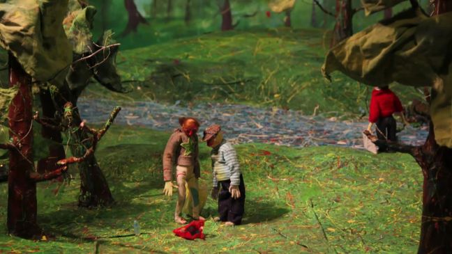 Zwei Figuren schauen auf eine am Boden liegende Tüte, im Hintergrund ein Fluss