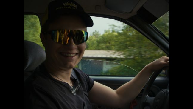 Ein Jugendlicher lächelnd mit Sonnenbrille im Auto