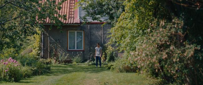 Miia steht im Garten, den Blick nach unten, die Arme herabhängend