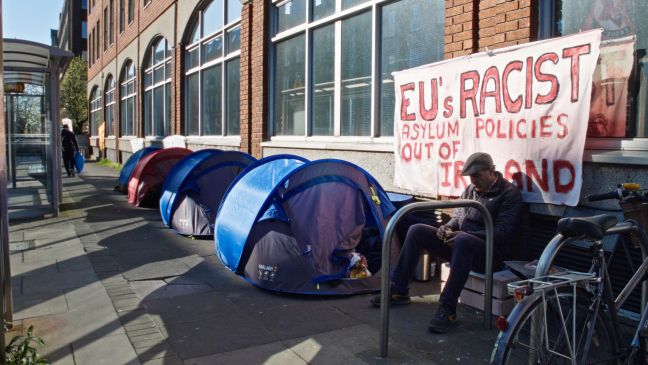 Zelte an einer Bushaltestelle mit einem Transparent "EU's racist asylum politics out of Ireland"