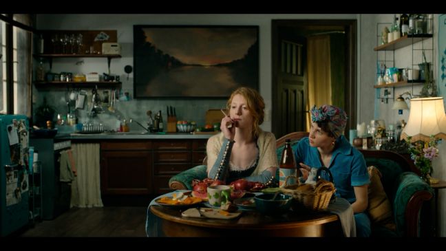 Nore und Jonna sitzen am Esstisch in der WG-Küche, Nore raucht und schaut nachdenklich