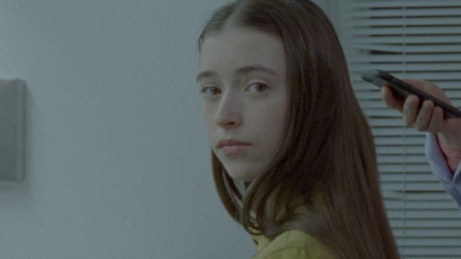 Eine junge Schauspielerin schaut in die Kamera, hinter ihr ein iPhone im Bild