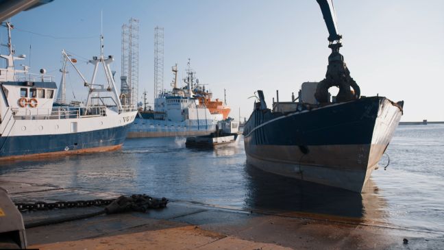 Ein Kran holt etwas vom Deck eines Trawlers, im Hintergrund weitere