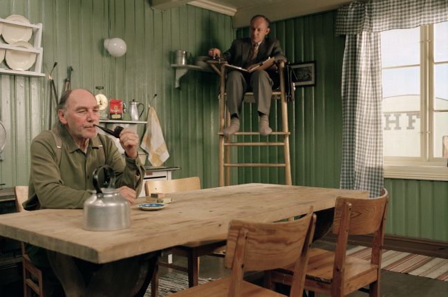 Isak sitzt an seinem Esstisch, raucht und wird beobachtet aus einem Hochstuhl