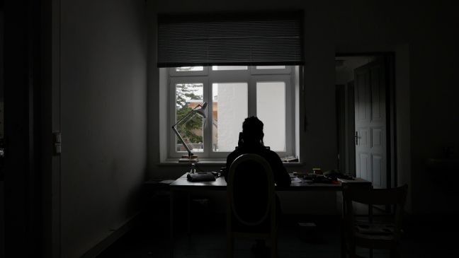 eine Person an einem Schreibtisch vor dem Fenster, telefonierend