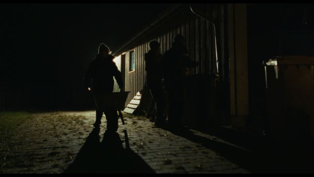 zwei Personen im Dunkeln mit einer Schubkarre vor einem Haus