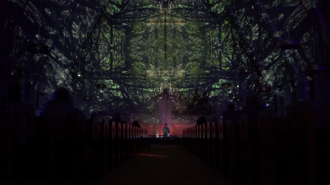 Veera Neva auf dem Boden der Bühne, über ihr ein Geäst auf die Kirchenwand projiziert