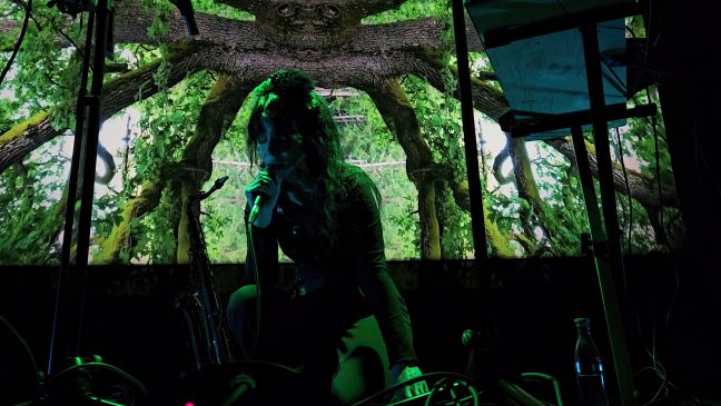 Veera Neva kniet leidenschaftlich singend vor der Leinwand, worauf das innere der Baumkrone gezeigt wird