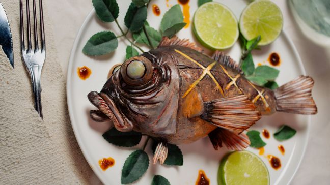 Ein gebackener Fisch liegt auf einem Teller, mit Limetten garniert