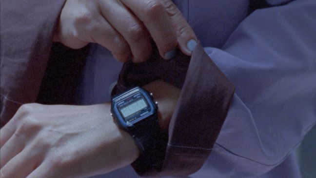 Eine Schauspielerin mit violettem Mantel schaut auf ihre Casio Digitalarmbanduhr