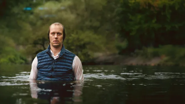 ein bekleideter Mann, klitschnass in einem Teich