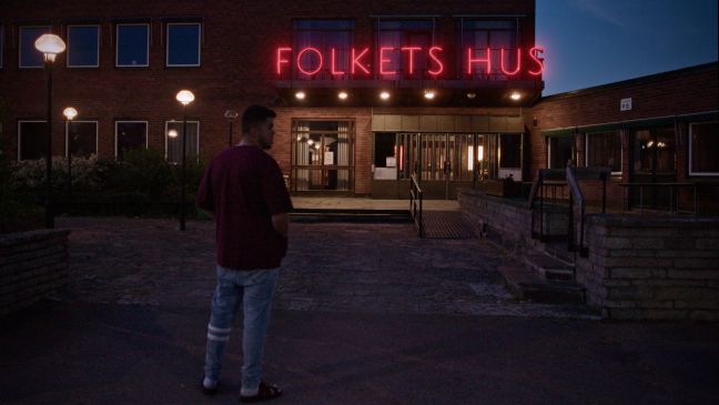 Majd bei Nacht vor dem Gemeindehaus, welches mit rotem Neonschild beleuchtet ist