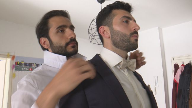 Alayham im Anzug, bekommt die Fliege von seinem Bruder Obey gebunden