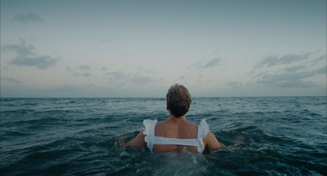 Paul schwimmt im Meer im weißen Sommerkleid