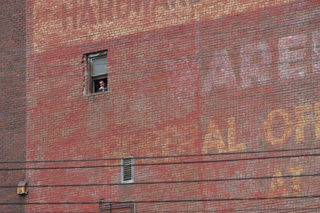 Hank schaut aus dem einzigen Fenster einer großen Backsteinmauer