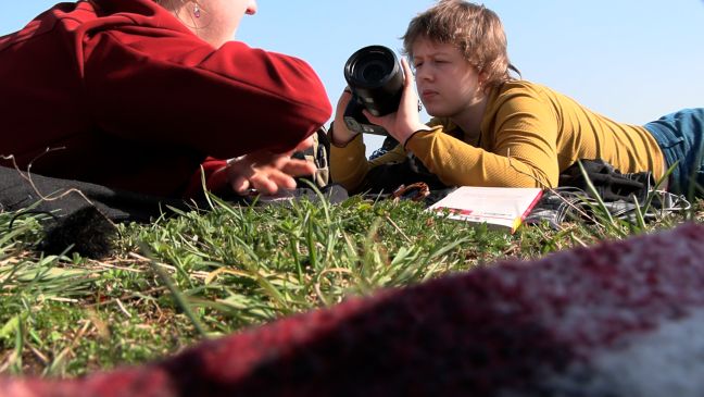 Roosi auf der Wiese fotografiert jemanden mit einer Kamera von unten