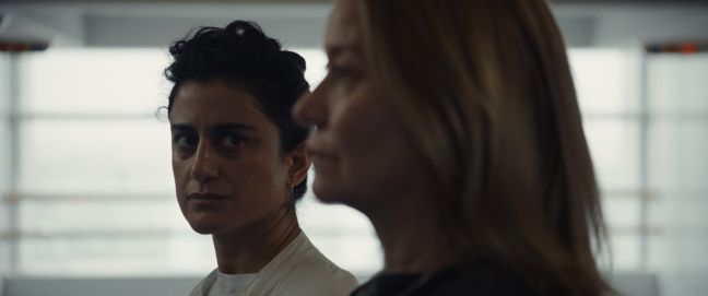 Alex im Hintergrund, guckt Camilla an; beide schauen ernst