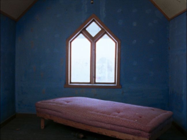ein blaues Zimmer mit einem spitzen Fenster und einem rosa Bett