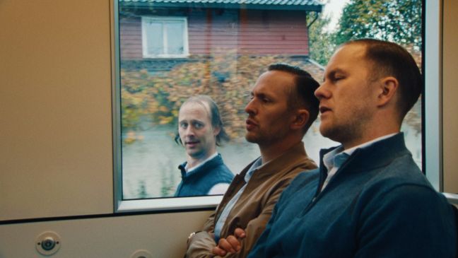 zwei Männer in der Straßenbahn und ein dritter vor dem Fenster