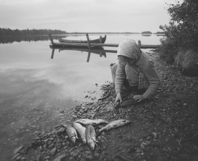 Kind am Seeufer, mit gefangenem Fisch neben sich