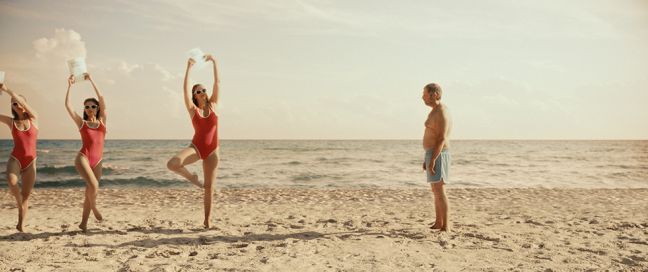 drei Frauen in roten Badeanzügen machen Sport am Strand, ein Mann schaut ihnen zu