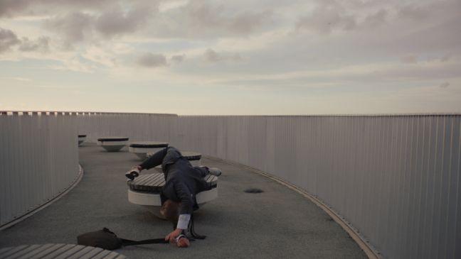 Der Mann liegt verrenkt auf dem Oberdeck auf einer runden Sitzmöglichkeit