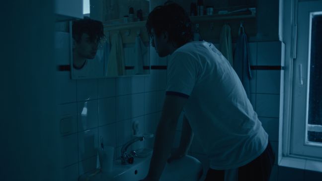 Samir schaut nachts mit nassen Haaren ernst in den Spiegel