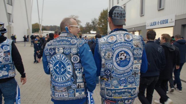 Zwei Fans des SV Darmstadt '98 stehen mit Fußball-Jeanskutten vor dem Stadion
