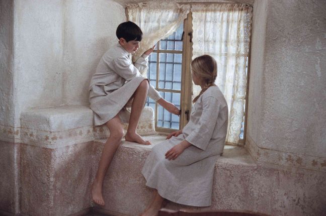 Fanny und Alexander sitzen in Gewändern vor einem Fenster