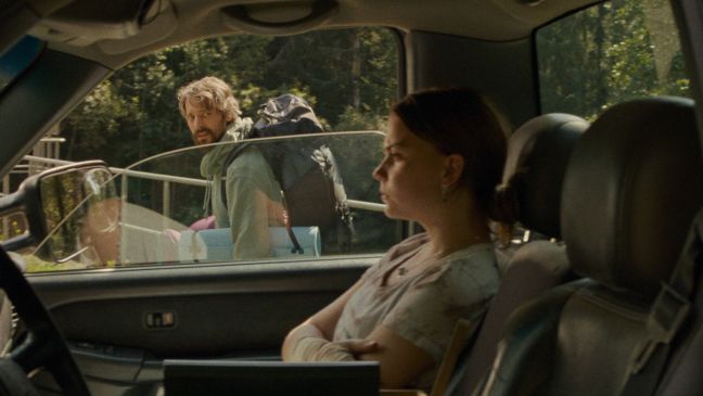Lise sitzt im Auto und Olof trägt die Campingsachen