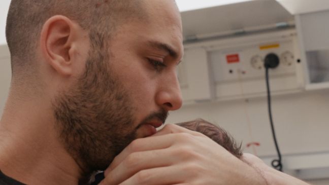 David hält den Kopf des Säuglings nah an seinen Kopf