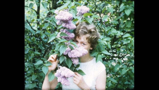 Monika als junge Frau,versteckt ihr Gesicht hinter rosa blühendem Flieder