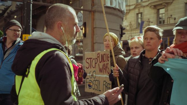 Ein Dialogpolizist mit Kopfhörern im Ohr gegenüber von Demonstranten